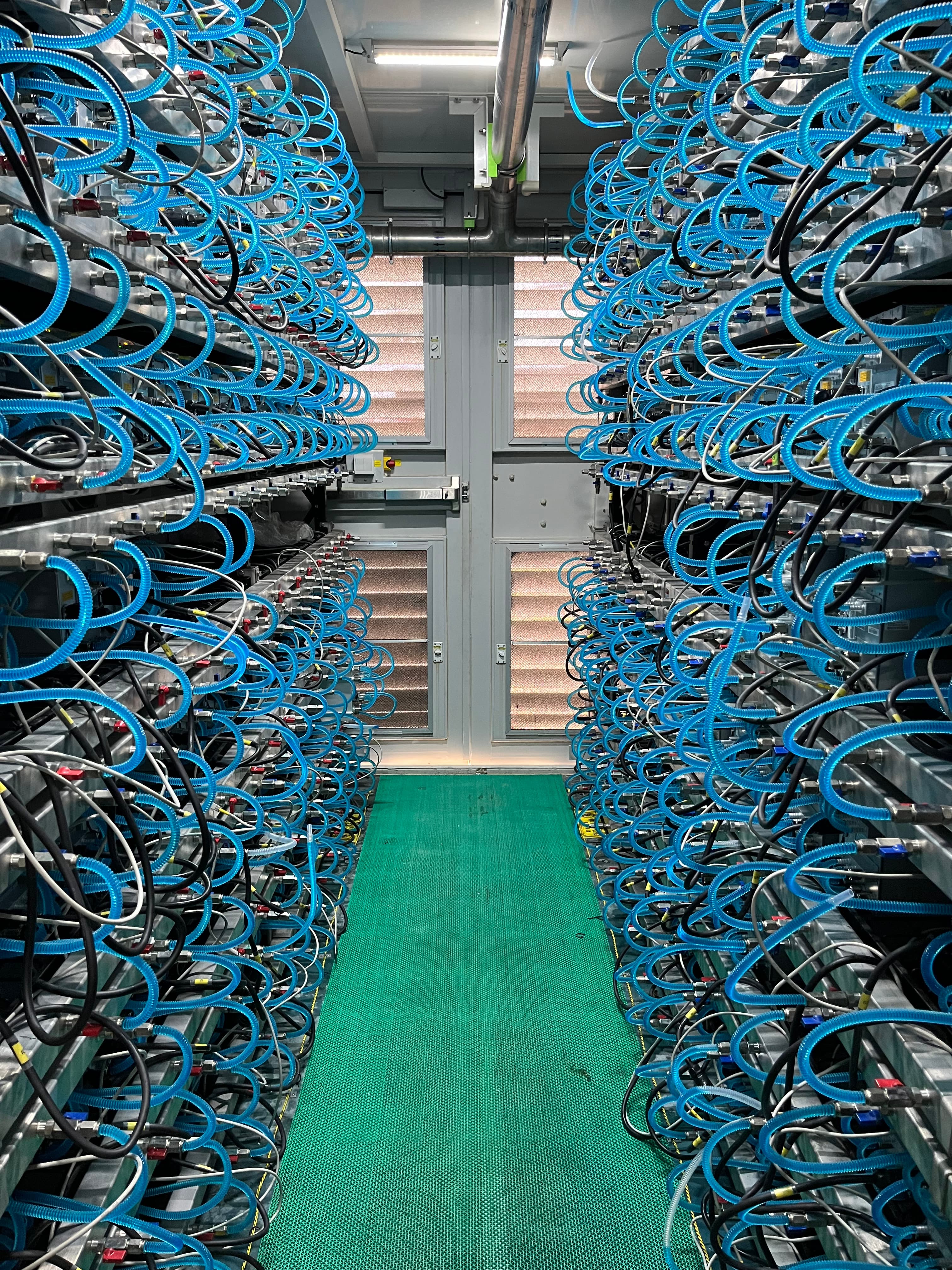 Interior aisle of liquid-cooled racks with blue coolant hoses and green floor mat