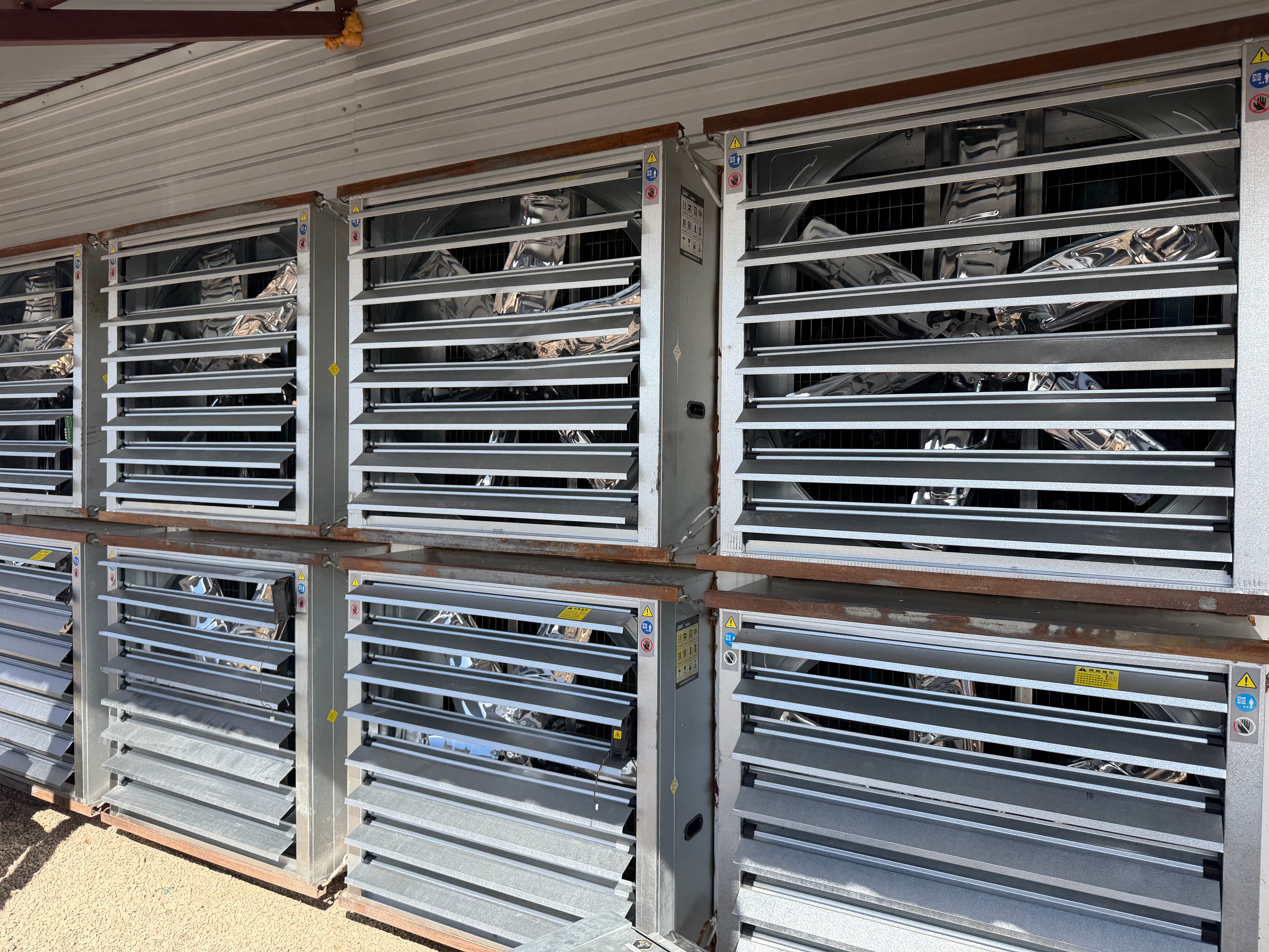 Wall-mounted industrial exhaust fans with metal louvers under a corrugated roof