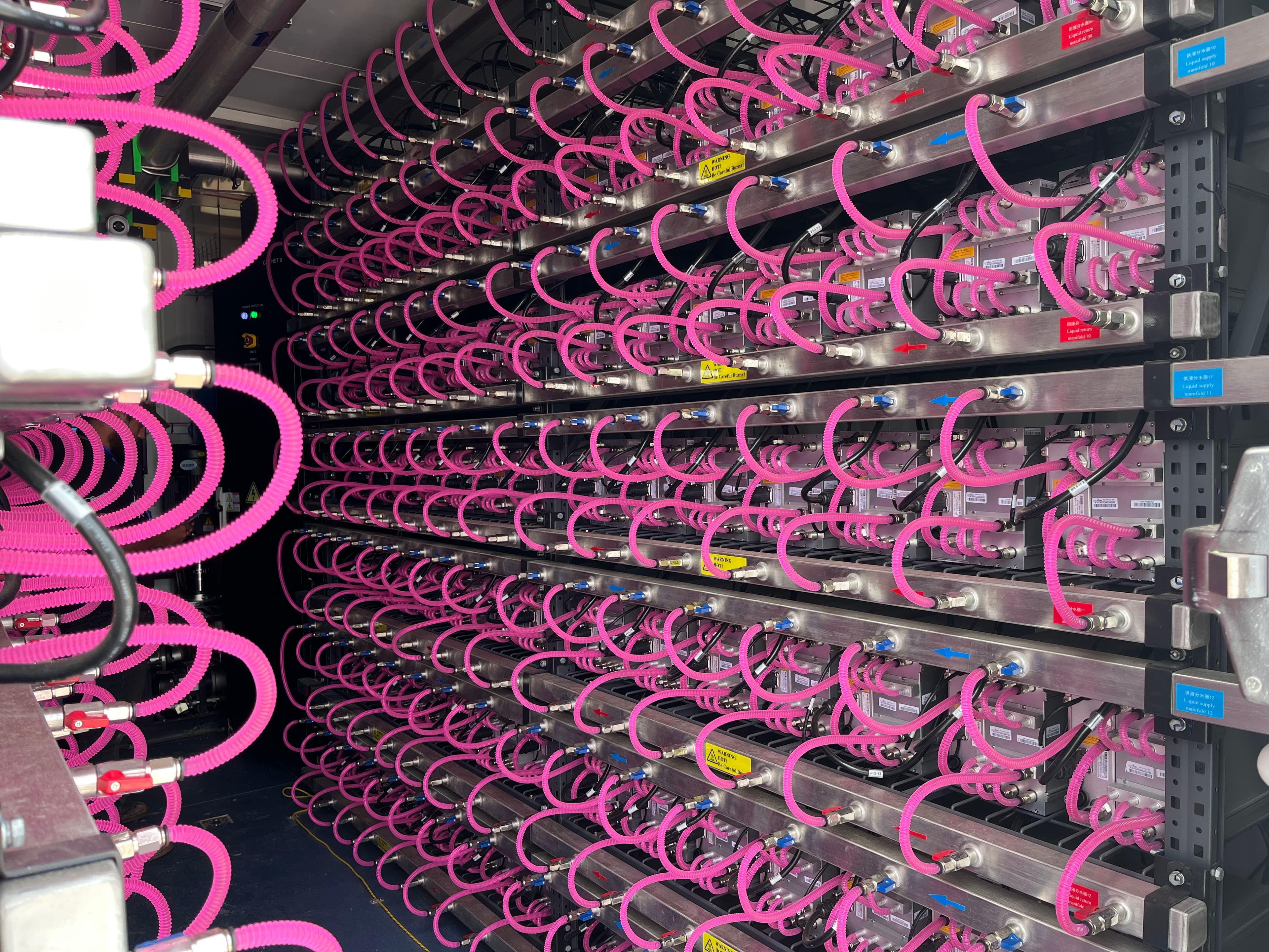 Close-up of hydro-cooled modules with pink corrugated coolant hoses in a rack