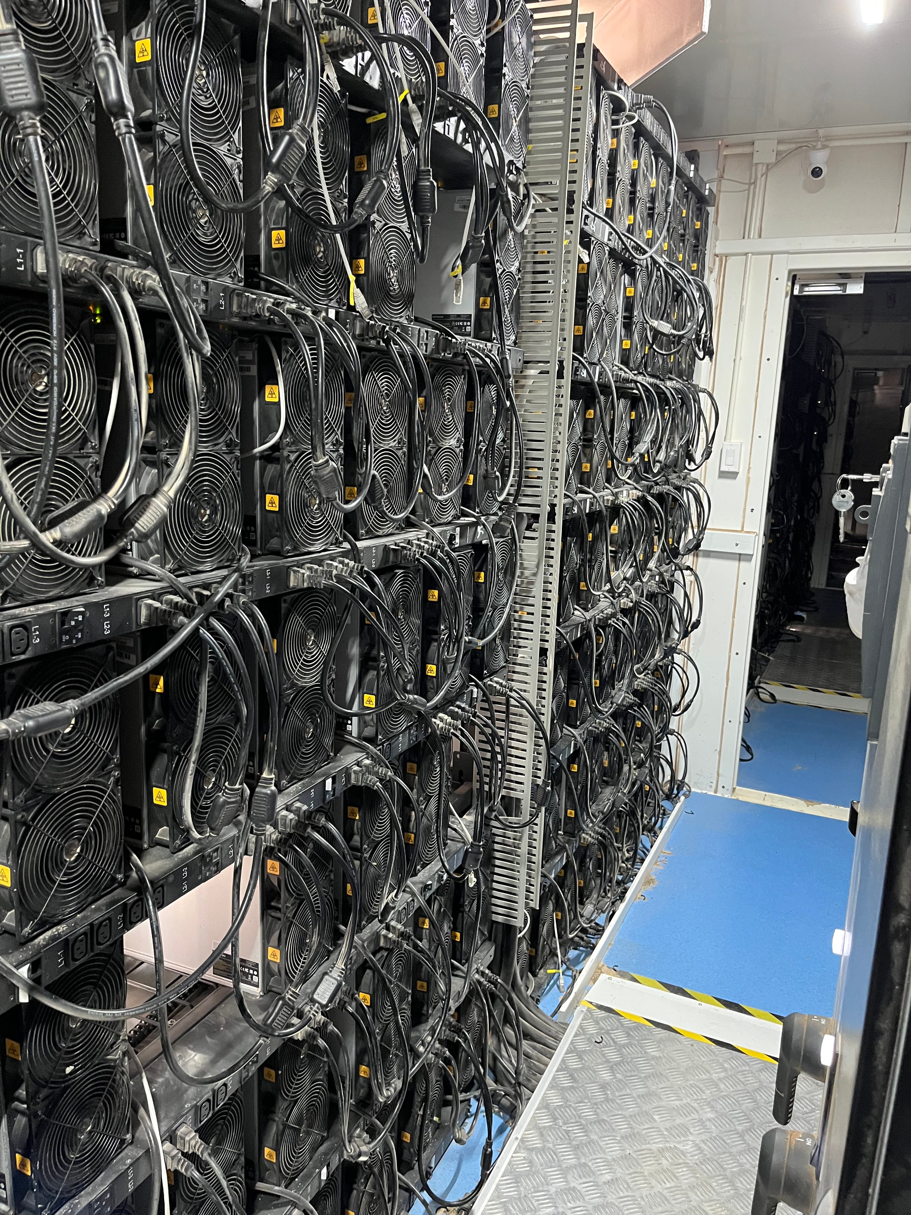 Dense racks of air-cooled ASIC miners with power cabling in a white-walled room