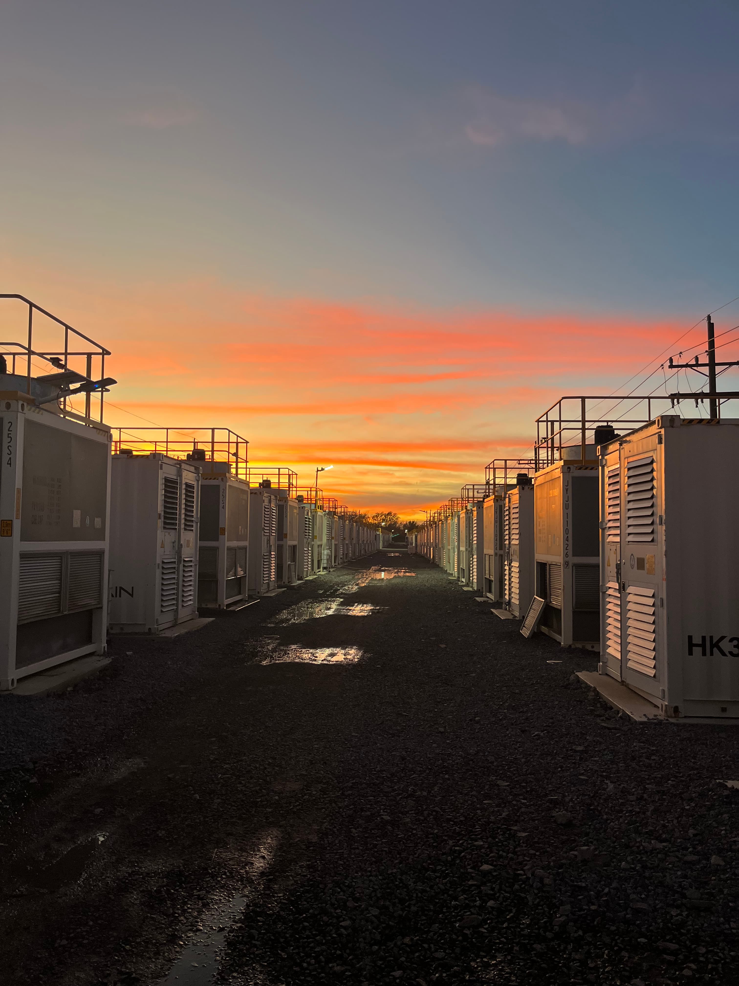 Two rows of white modular containers at sunset along a gravel access lane