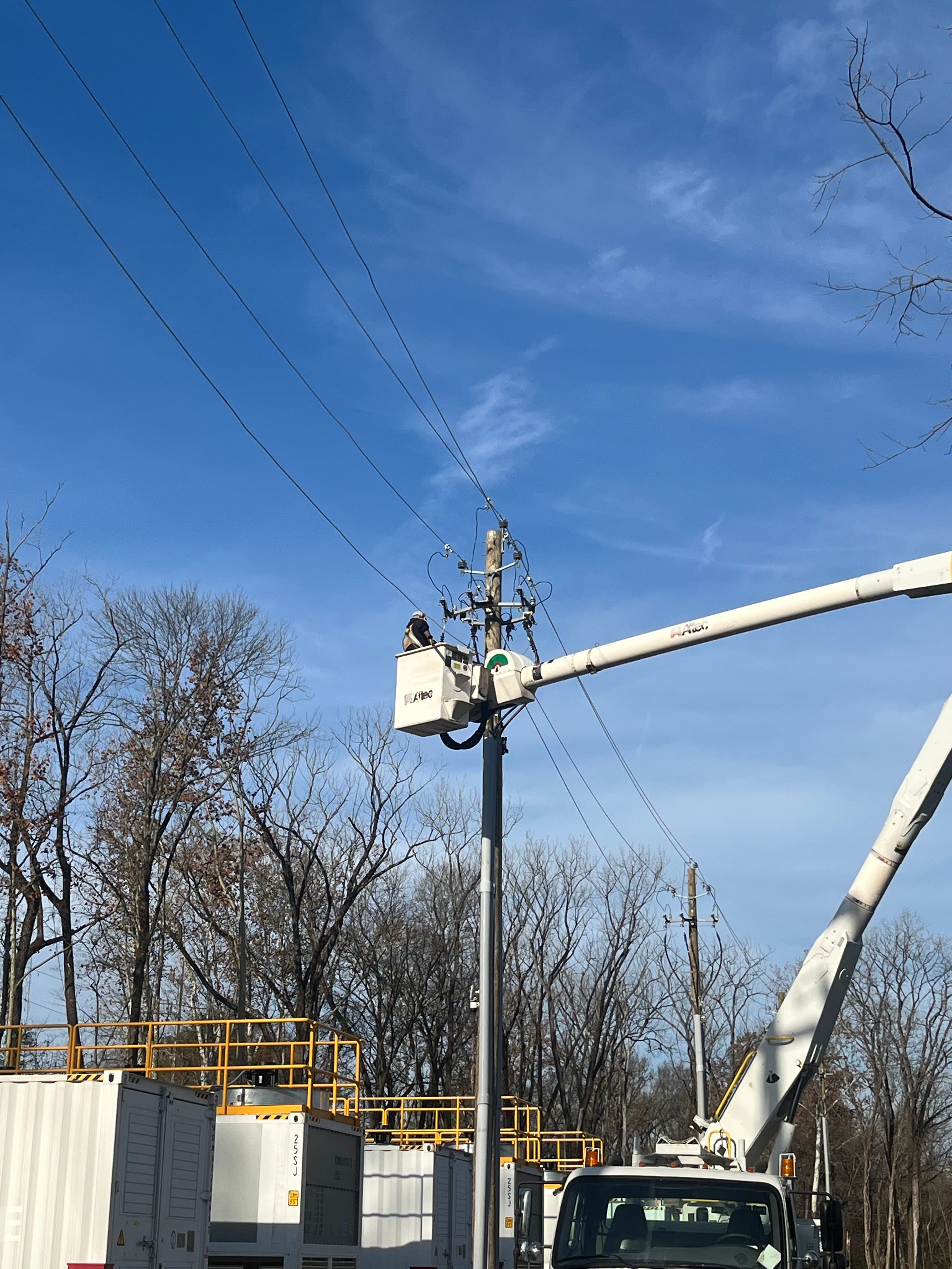 Lineworker in a bucket truck servicing overhead lines above containerized equipment